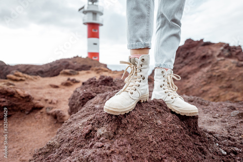 Traveler standing on the rocky land, traveling volcanic landsacpes near the lighthouse. View on the woman's trekking shoes photo