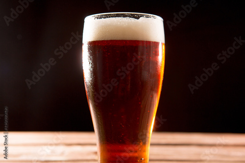Cold tasty beer on a hot summer day. Glass of beer on wooden table on black background