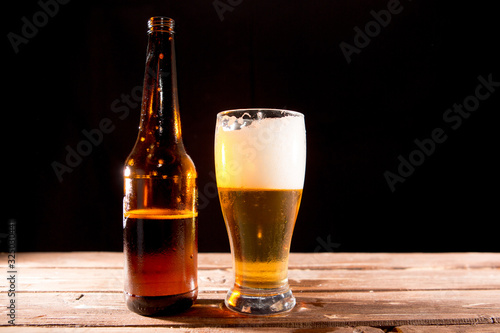 Cold tasty beer on a hot summer day. Glass and bottle of cold beer with foam on wood table with wood background