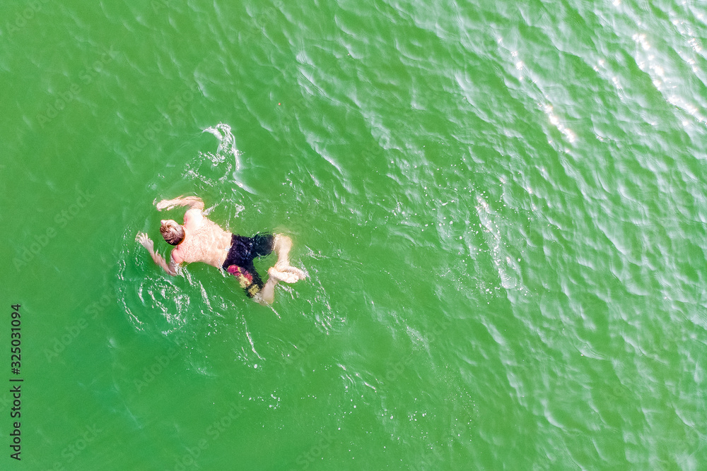 Aerial view of man floating on seawater enjoying vacations in tropical place.