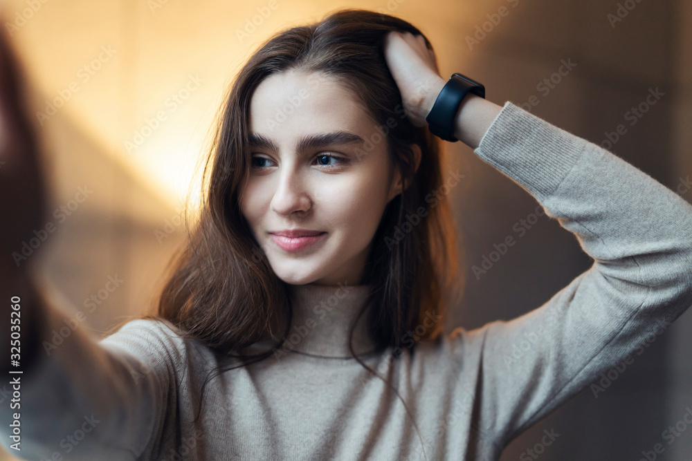 Fototapeta premium Beautiful young smiling woman is looking the camera. Model posing in front of the camera during photo shooting. Millennial girl taking selfie for social networks to share it with friends.