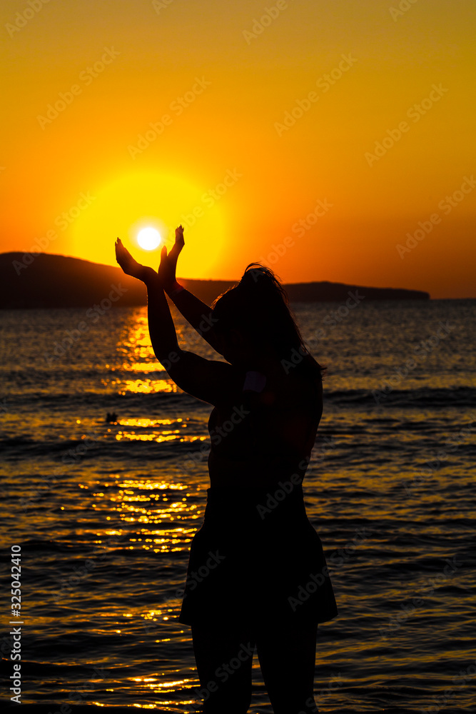 The girl holds the sun in her hands. Beautiful sunrise on the sea.