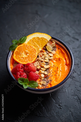 Bowl with fresh healthy smoothie or yogurt. With orange slices, tangerine, raspberry, chia and nuts