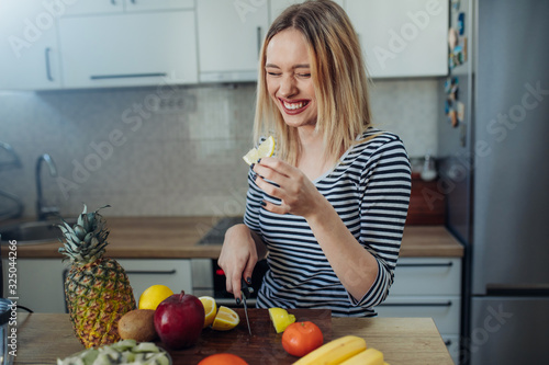Happy healthy woman cutting fruits on a wooden board while making breakfast in a kitchen