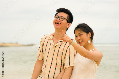 sweet and romantic lifestyle portrait of young happy Asian Korean couple in love enjoying holiday on beautiful beach walking together by the sea playful and affectionate
