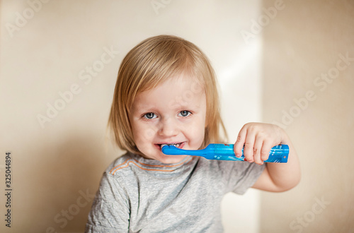 The boy is brushing his teeth. Toddler with blond long hair and dental health