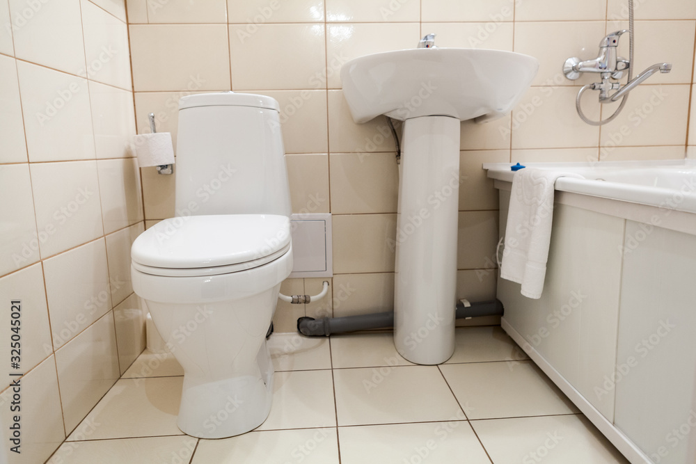 Interior of simple half bathroom with toilet, sink and bath with shower, white sanitary ware Interior of simple half bathroom with toilet, sink and bath with shower, white sanitary ware