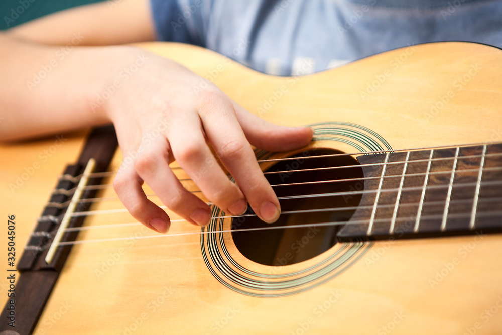Fototapeta premium Female hand plucks the strings of a yellow acoustic guitar, close up view