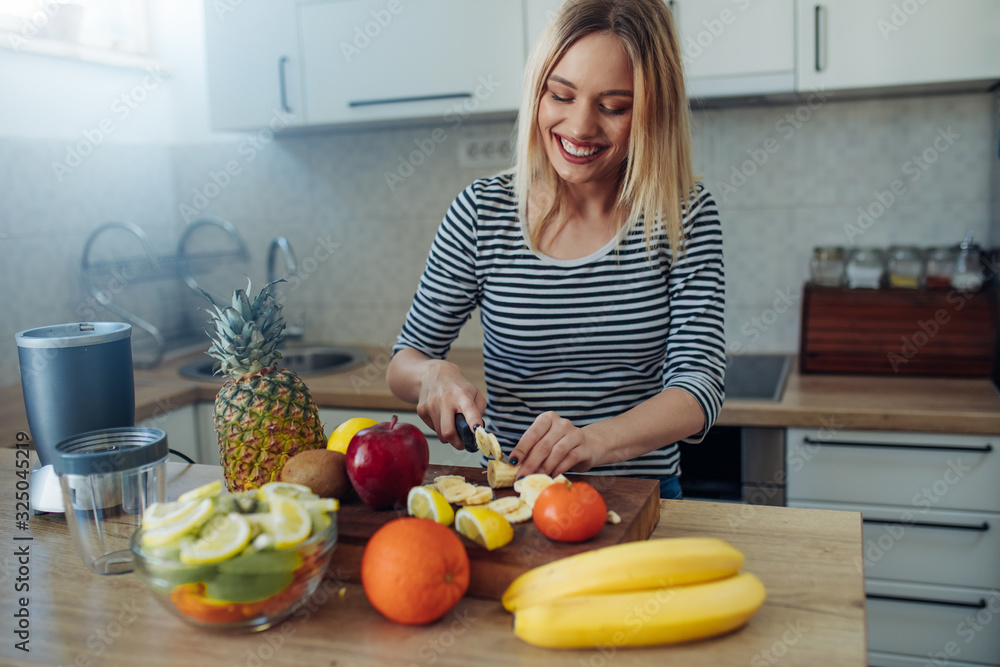 Happy healthy woman cutting fruits on a wooden board while making breakfast in a kitchen