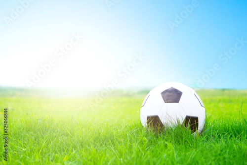 Soccer ball on a green lawn close up against clear blue sky and sun