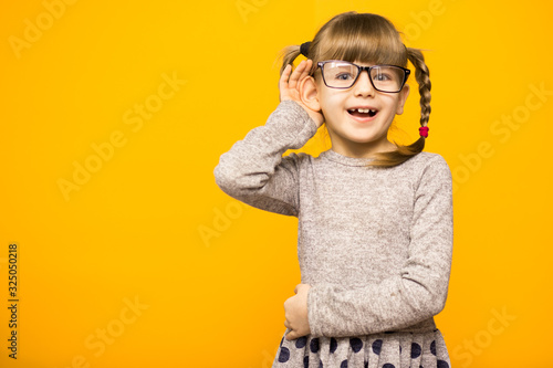 Quadro su tela A young child girl journalist in glasses with funny pigtails listening to someth