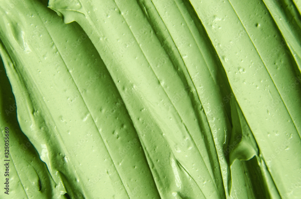 Green cosmetic clay (cucumber facial mask, avocado face cream, green tea body wrap) texture close up, selective focus. Abstract background with brush strokes