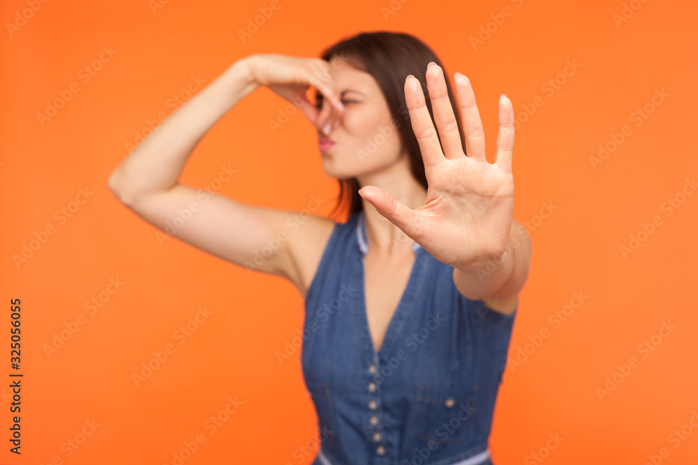 Awful odor, stink. Confused woman pinching nose and gesturing stop, ignoring bad breath, disgusting smell of farting, her grimace expressing repulsion, gross. studio shot isolated on orange background Awful odor, stink. Confused woman pinching nose and gesturing stop, ignoring bad breath, disgusting smell of farting, her grimace expressing repulsion, gross. studio shot isolated on orange background