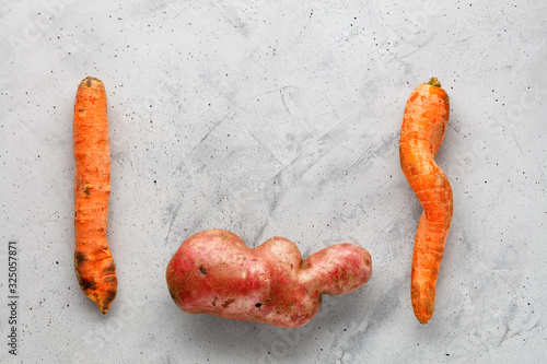Ugly potato in the letter shape and twisted carrot on a background of gray concrete. Vegetable or food waste concept. Top view, close-up.
