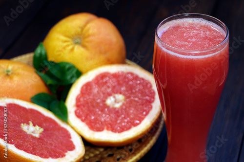 A glass of fresh grapefruit juice and grapefruit fruits on a wooden table. Healthy food.  