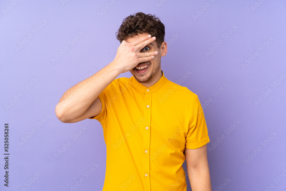 Caucasian man isolated on purple background covering eyes by hands and smiling Caucasian man isolated on purple background covering eyes by hands and smiling