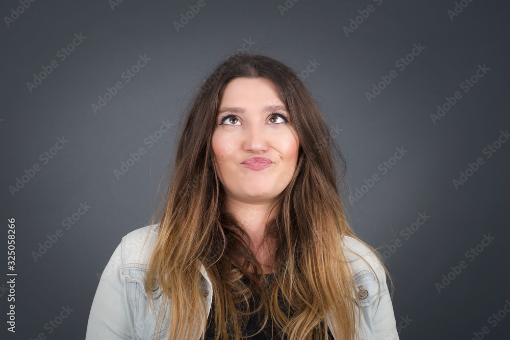 Funny comic girl crosses eyes, puts lips, makes grimace, foolishes after all day studying. Clueless woman nerd with awkward expression has fun alone, plays fool. Wears white sweater Funny comic girl crosses eyes, puts lips, makes grimace, foolishes after all day studying. Clueless woman nerd with awkward expression has fun alone, plays fool. Wears white sweater
