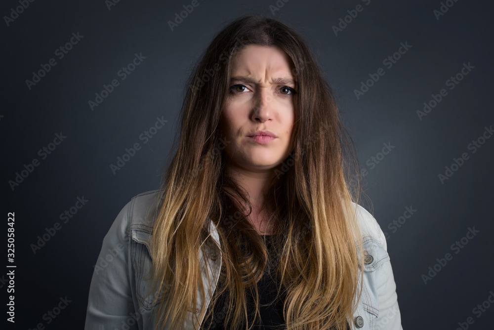 Portrait of outraged young woman with oval face, blue eyes and long hair wearing White sweater frowning her eyebrows being displeased with something. Scowling pretty female isolated over grey.� Portrait of outraged young woman with oval face, blue eyes and long hair wearing White sweater frowning her eyebrows being displeased with something. Scowling pretty female isolated over grey.�