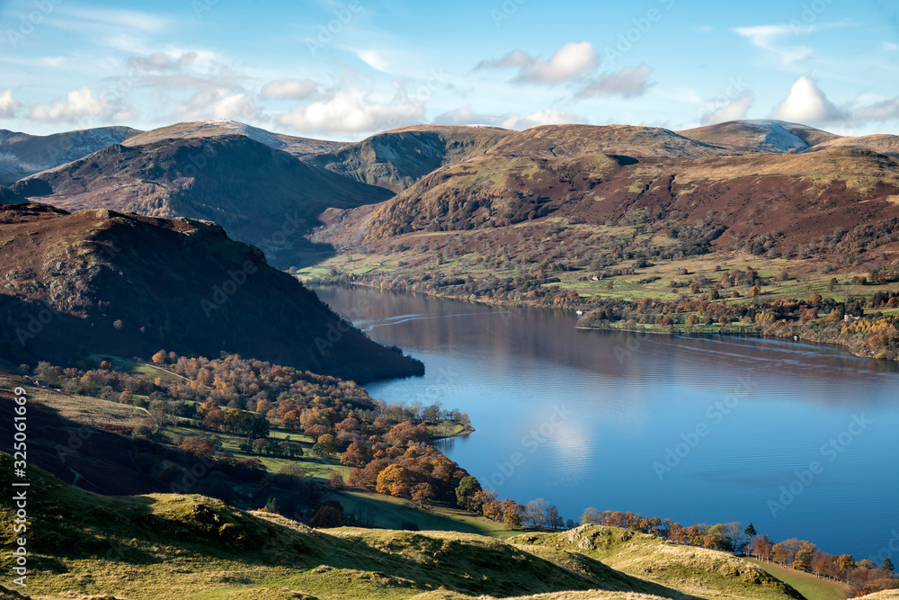 Beautiful Autumn Fall landscape of Ullswater and surrounding mountains and hills viewed from Hallin Fell on a crisp cold morning with majestic sunlgiht on the hillsides