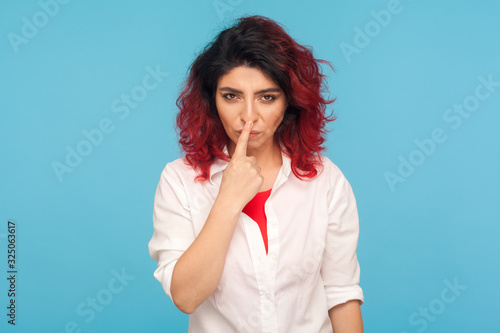 Falsehood sign. Portrait of angry displeased woman with fancy red hair in white shirt touching nose with lie gesture, blaming for deceit, forgery. indoor studio shot isolated on blue background