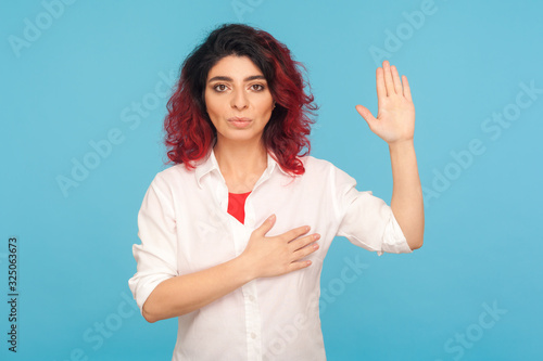Foto I swear! Portrait of hipster woman with fancy red hair holding hand on heart and raising palm to make oath, devoting herself, promising to fulfill task responsibly