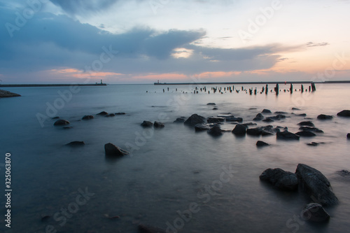 Beautiful long exposure beach landscape with rocks and remains of poles in water