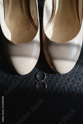 Beige women shoes and golden wedding rings on black background, copy space. Wedding concept. Top view, flat lay