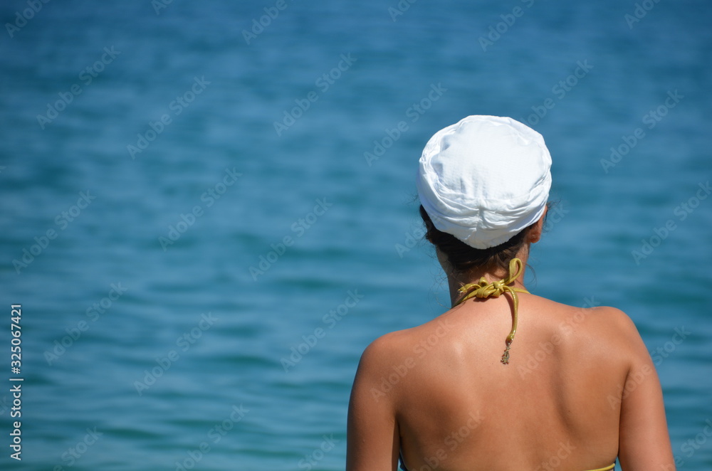 A young woman in a white headdress in a bikini swimsuit is waist-deep in the sea. beautiful sunny summer day
