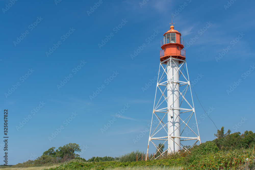 Landscape of lighthouse with red top and white base with green grass and blue sky background and copy space. Pape Lighthouse.