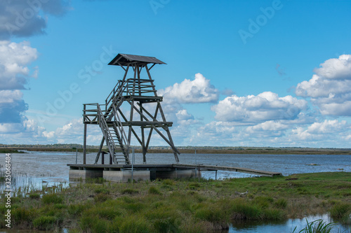 Floating wooden viewing tower on water. Engure Lake Nature Park, Latvia. Cloudy blue sky background