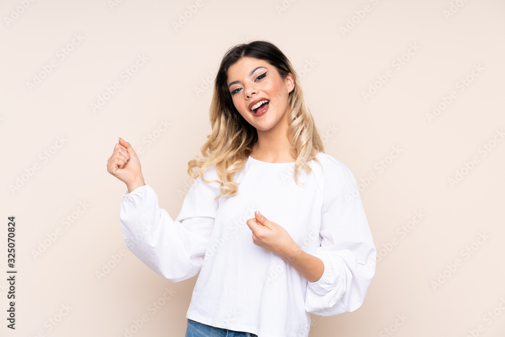 Teenager girl isolated on beige background making guitar gesture Teenager girl isolated on beige background making guitar gesture