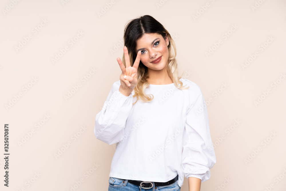 Teenager girl isolated on beige background happy and counting three with fingers Teenager girl isolated on beige background happy and counting three with fingers