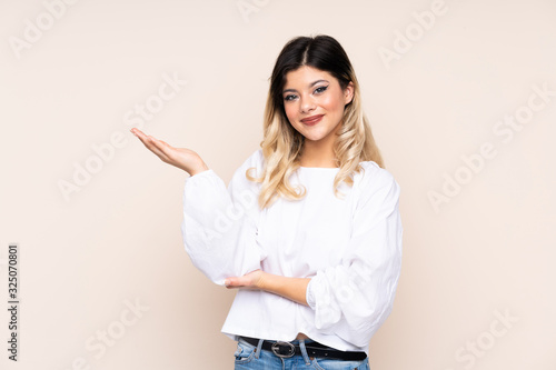 Teenager girl isolated on beige background extending hands to the side for inviting to come