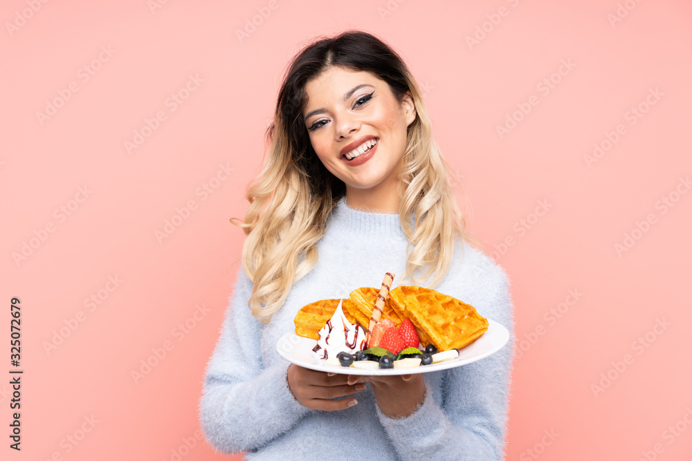 Teenager girl holding waffles on isolated pink background smiling a lot Teenager girl holding waffles on isolated pink background smiling a lot