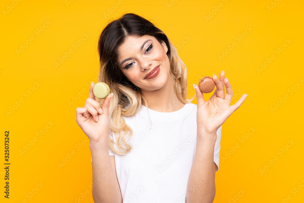 Teenager girl isolated on yellow background offering colorful French macarons Teenager girl isolated on yellow background offering colorful French macarons