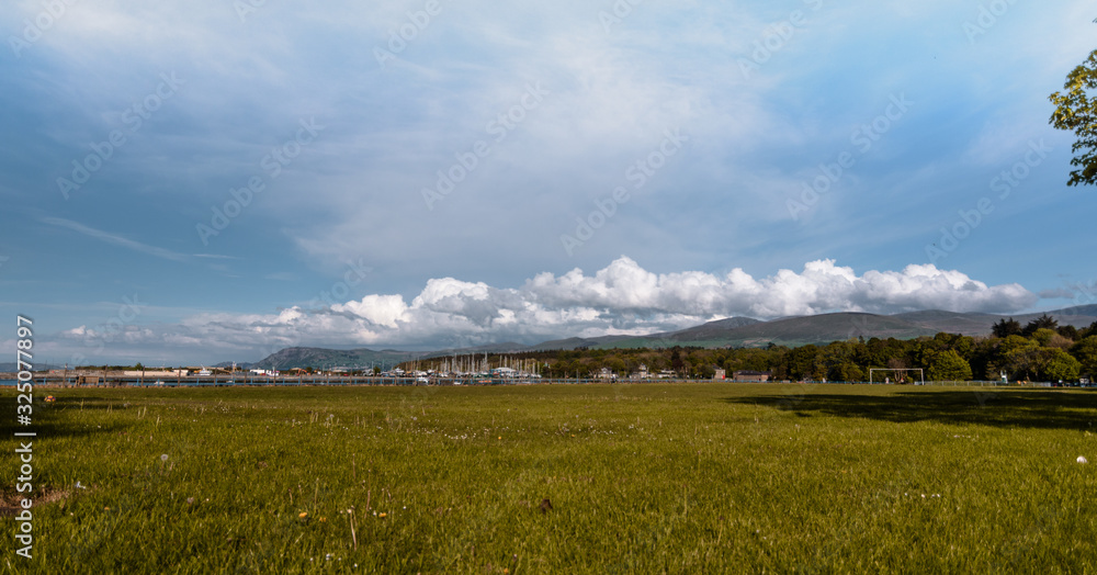 Grassland and a harbour with a background of mountains, clouds and blue sky