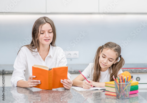 Photo Young mom helps daughter do schoolwork at home