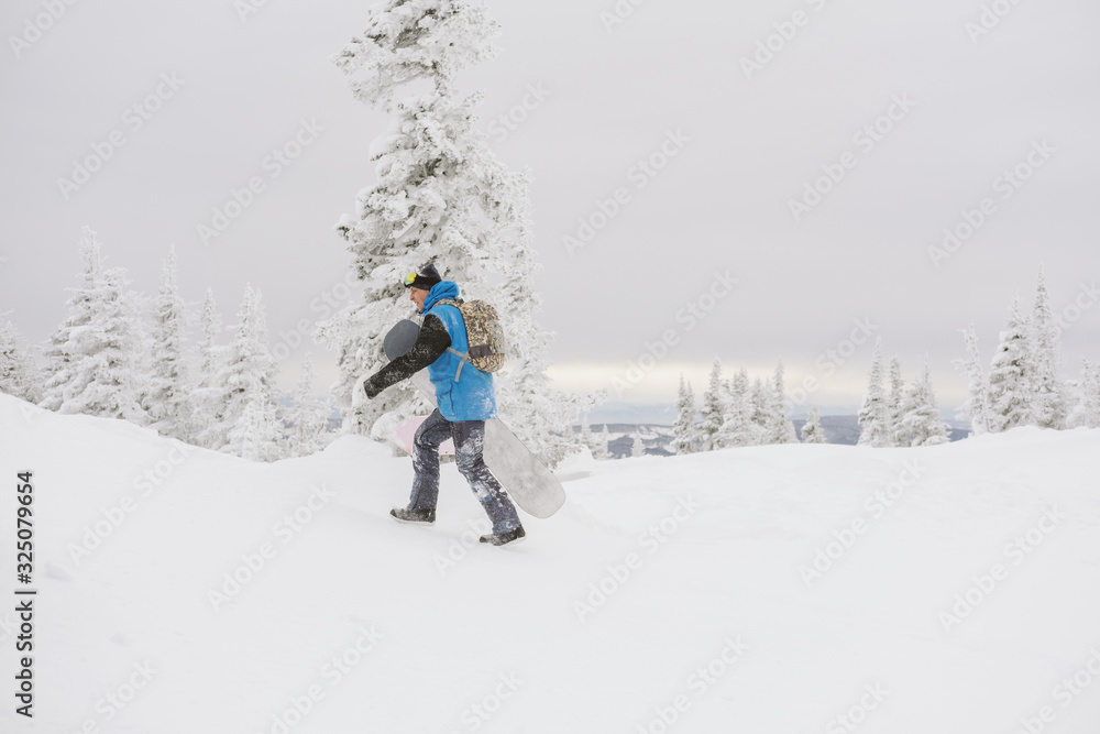 Snowboarder free rider  man walking on snowy slop, snow covered trees on background, bad weather, siberian winter snow powder day in ski resort