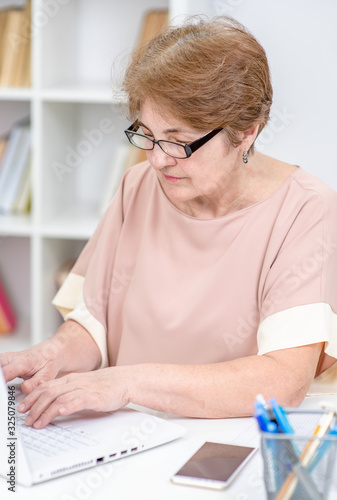Elderly woman works on laptop in the office