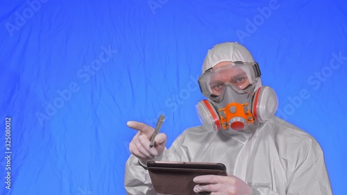 Scientist virologist in respirator makes write in an tablet computer with stylus. Man wearing protective medical mask. Chroma key blue. photo