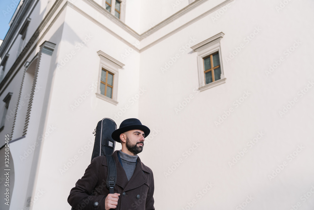 Naklejka premium Portrait of male artist walking with guitar on the street