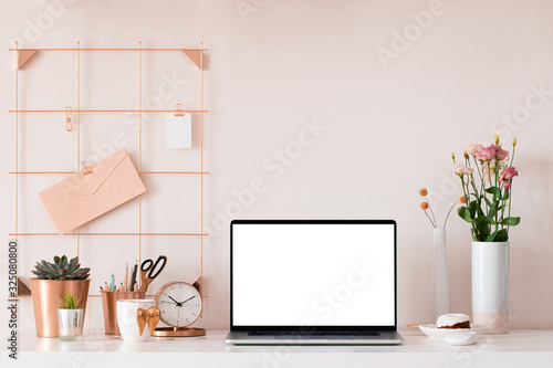 Laptop with blank white screen on office desk interior. Stylish rose gold workplace mockup table view. photo
