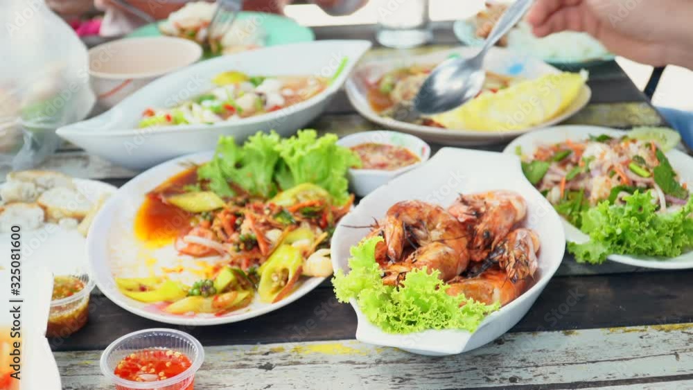 Closeup view and overexposed. Grilled shrimp and seafood in plate placed on wooden table of restaurants by the sea. With hands blurred of people are scooping and picking food during the lunch. Closeup view and overexposed. Grilled shrimp and seafood in plate placed on wooden table of restaurants by the sea. With hands blurred of people are scooping and picking food during the lunch.
