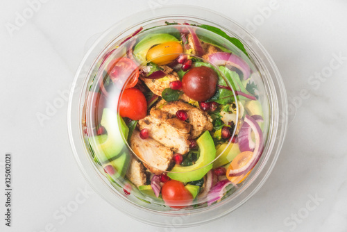 Plastic package with healthy chicken salad with avocado , tomatoes and pomegranate to take away