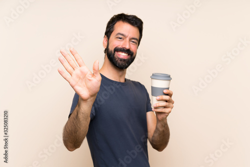 Man with beard holding a coffee saluting with hand with happy expression