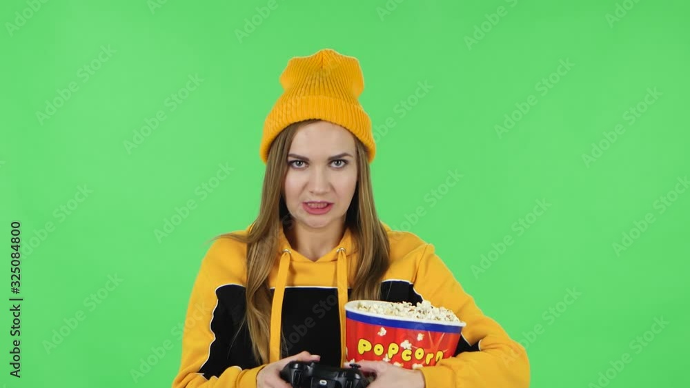 Portrait of modern girl in yellow hat with popcorn is playing a video game using a wireless controller. Green screen Portrait of modern girl in yellow hat with popcorn is playing a video game using a wireless controller. Green screen