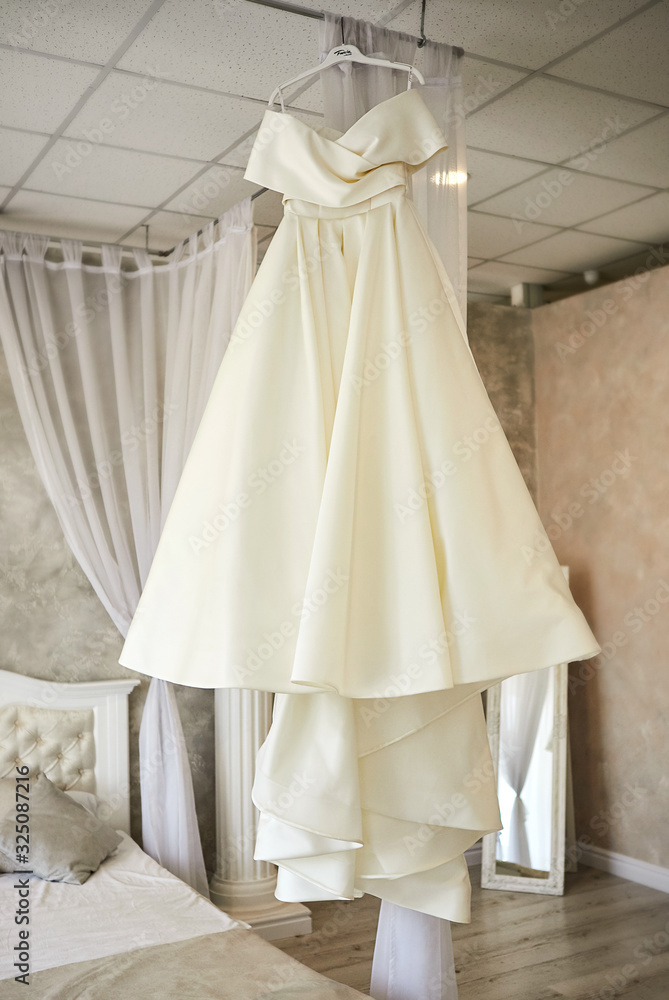 beautiful wedding dress hanging in the room, woman getting ready before  ceremony