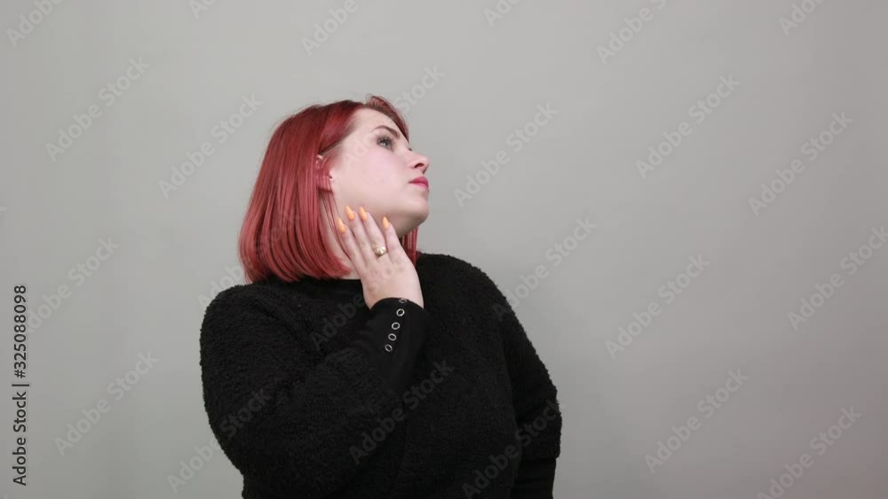 Young redhead fat lady in black sweater on grey background woman thinks, touches chin with hand Young redhead fat lady in black sweater on grey background woman thinks, touches chin with hand