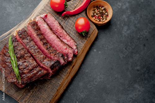 Beef steak on a cutting board with spices and tomatoes on a stone background with copy space for your text.