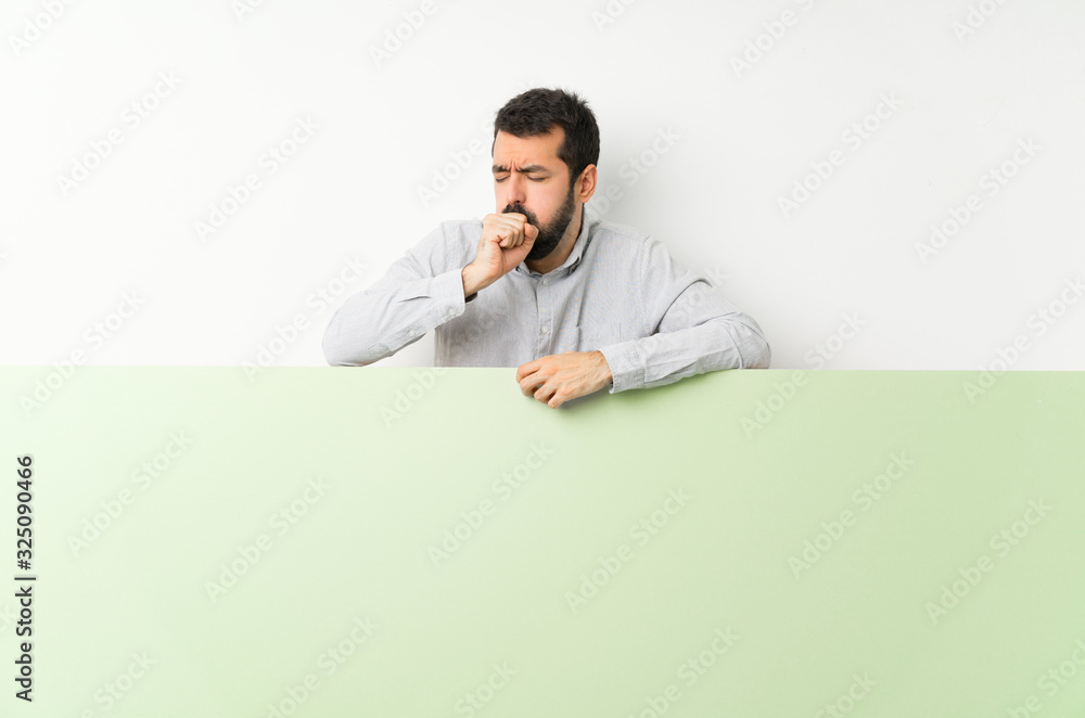 Young handsome man with beard holding a big green empty placard is suffering with cough and feeling bad Young handsome man with beard holding a big green empty placard is suffering with cough and feeling bad